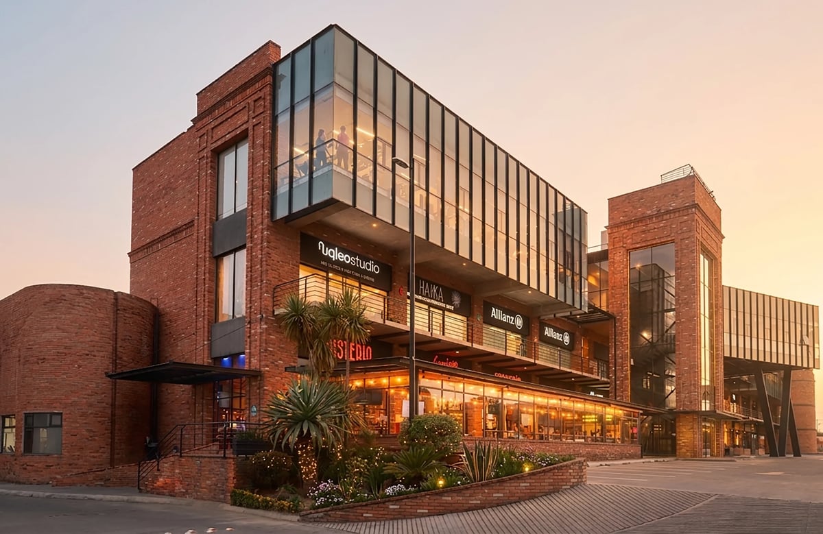 Modern brick building with glass storefront at dusk, featuring shops and restaurants at ground level